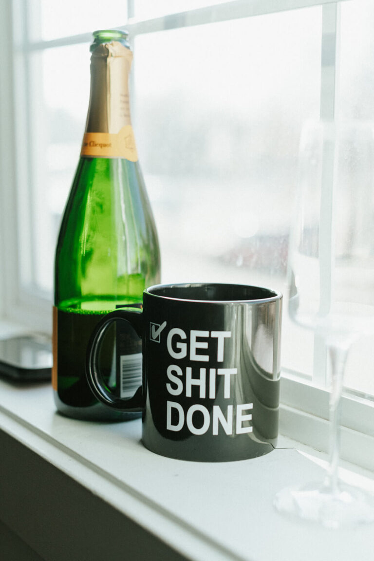 Bottle of wine in a window ledge with a coffee mug that says, "Get Shit Done"